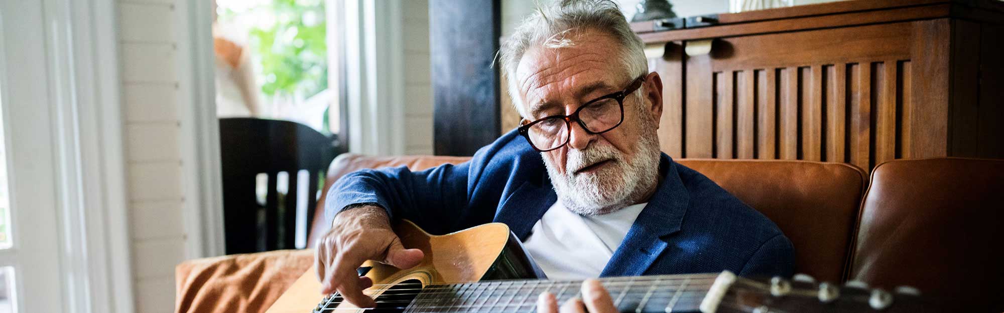 A man playing guitar in his apartment at Kingswood Senior Living Located in Kansas City, MO.