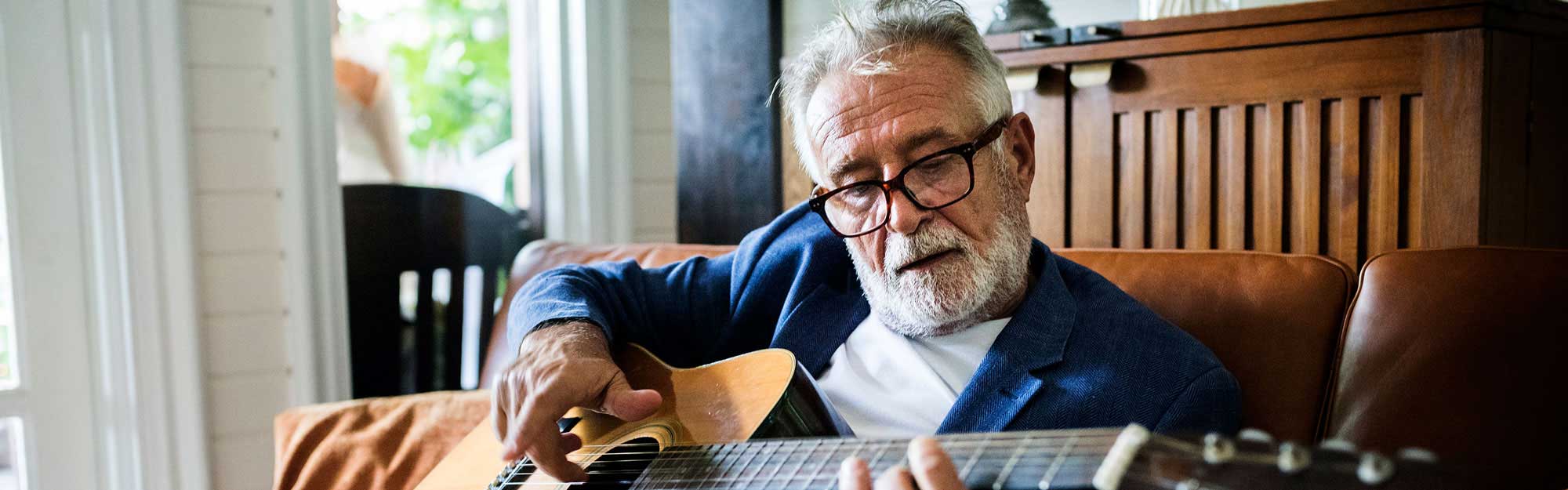 A man playing guitar in his apartment at Kingswood Senior Living Located in Kansas City, MO.