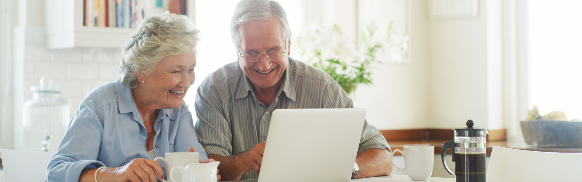 A couple looking over a computer and drinking coffee at Kingswood Senior Living Located in Kansas City, MO.